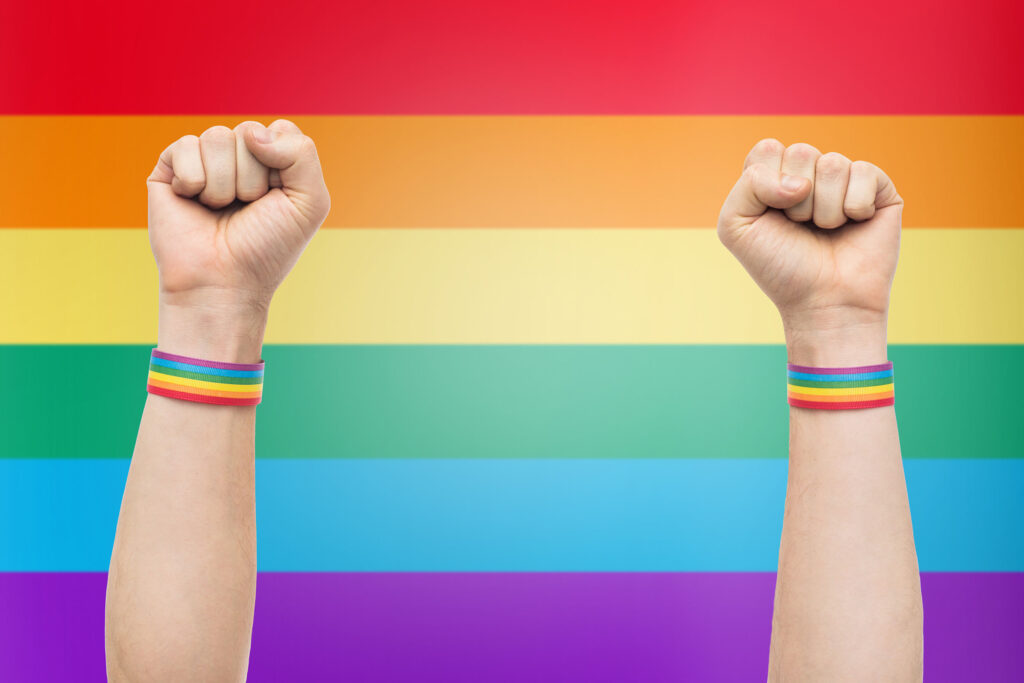 hands with gay pride rainbow wristbands shows fist